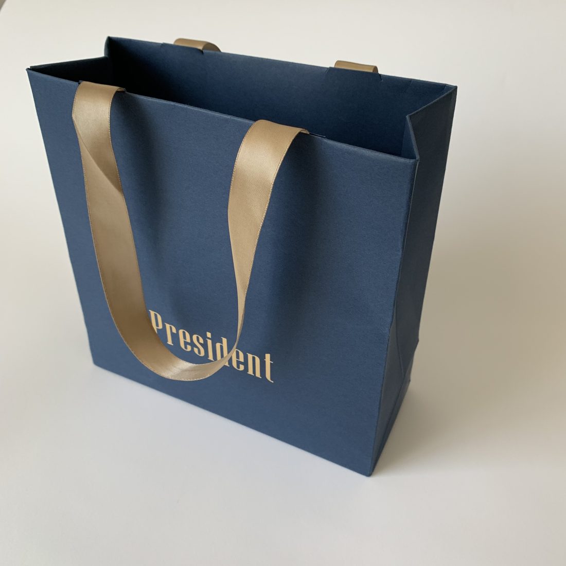 Navy art-paper carrier bag with ribbon handles and gold foil branding