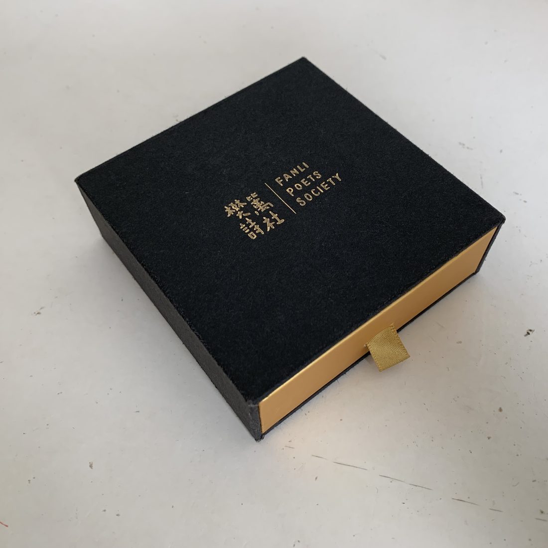 Black rigid lid-and-base gift box with gold foil logo, hand-wrapped at our plant